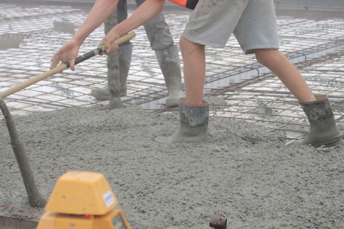 Concreters spreading wet concrete over steel mesh